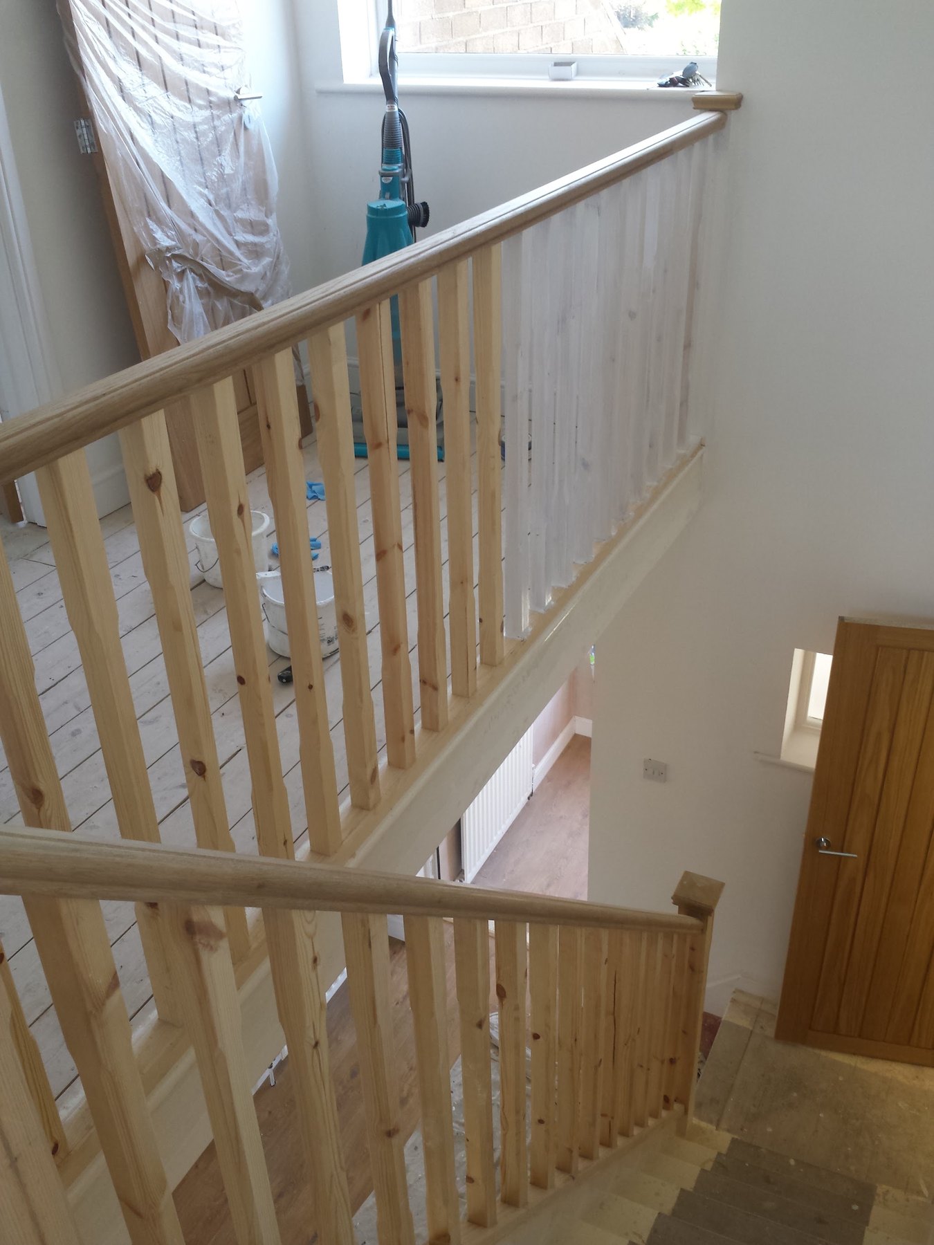 A landing with a new banister in bare pine and dust sheets hung at the window