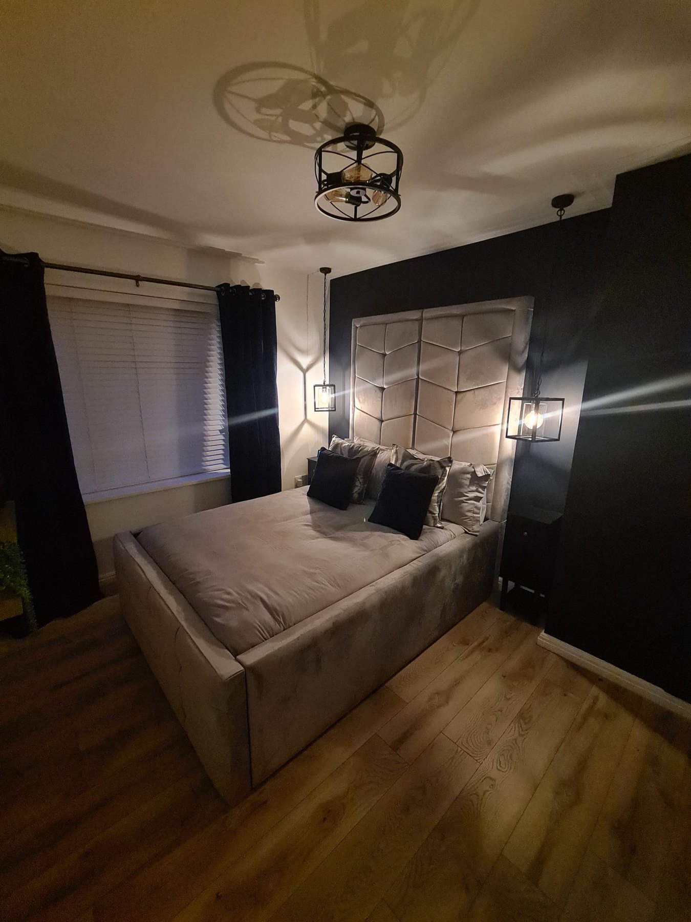 A bedroom with a black feature wall behind an upholstered bed