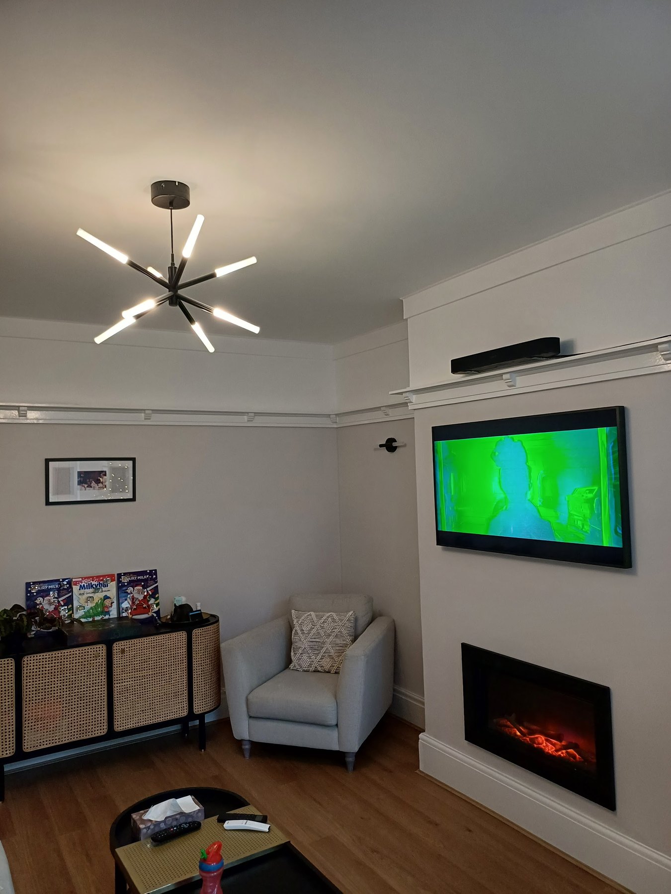 A lounge painted pale grey, with a television on the chimney breast above an electric fire