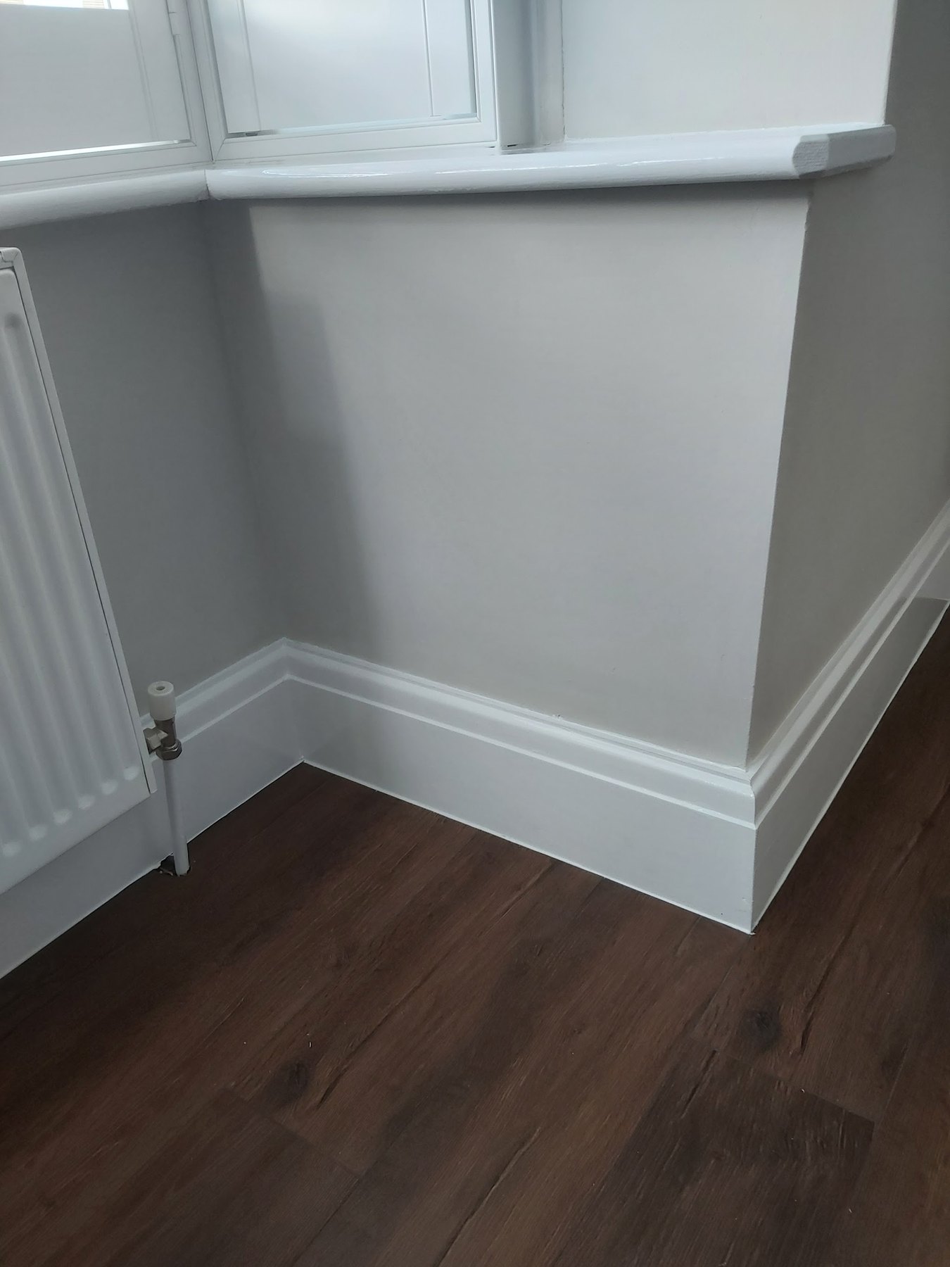 White skirting and a window board against a pale wall and a dark floor